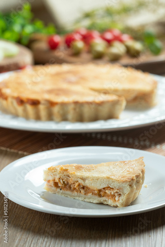 Chicken pie with cottage cheese, tomatoes, onion and olives on wooden table and white plate.