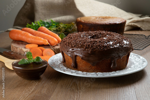 Brazilian carrot cake with chocolate frosting on wooden table with carrots in the background