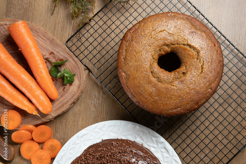 Brazilian carrot cake with chocolate frosting on wooden table with carrots in the background. Top view.