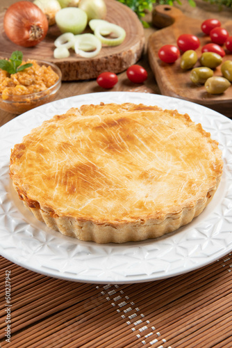 Chicken pie with cottage cheese, tomatoes, onion and olives on wooden table and white plate