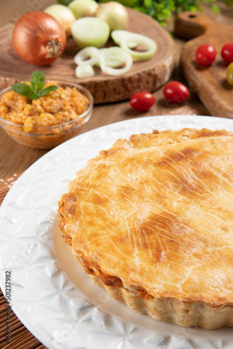 Chicken pie with cottage cheese, tomatoes, onion and olives on wooden table and white plate