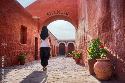Turista latina caminando de espaldas entrando al arco Silencio del monasterio Santa Catalina en Arequipa photo