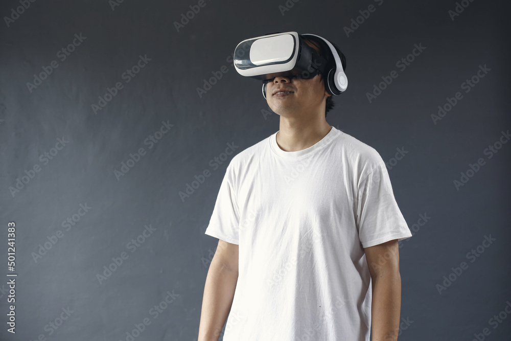 Young man using VR glasses and headset againts dark grey background. Young man using VR glasses and headset againts dark grey background.