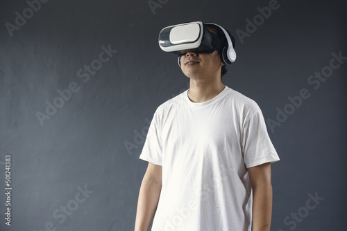Young man using VR glasses and headset againts dark grey background. 