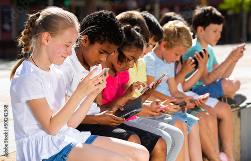 Group of positive kids sitting at urban street with mobile devices