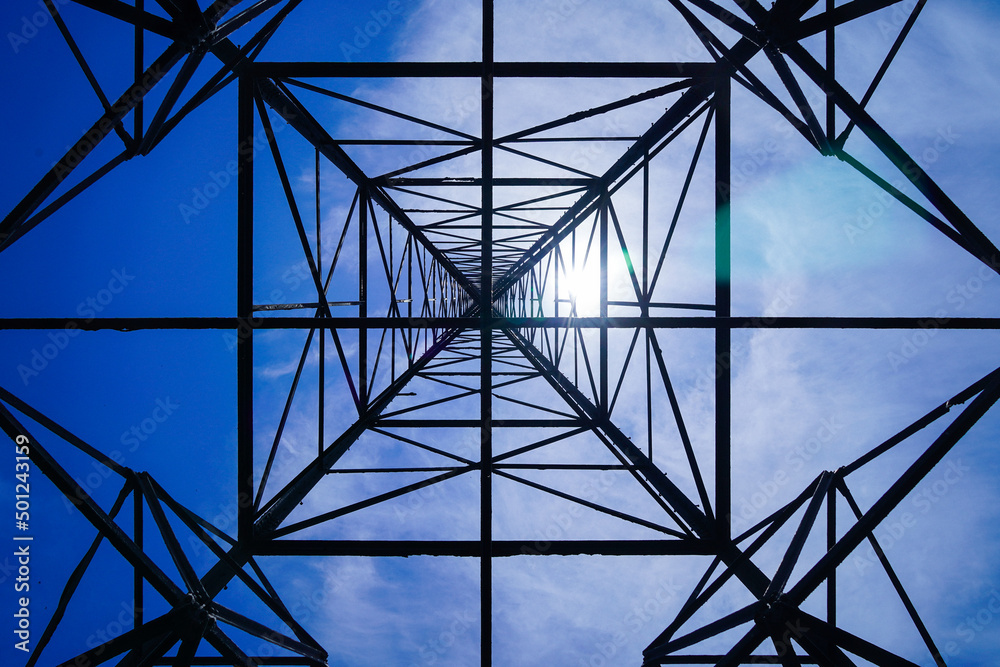 High voltage tower on blue sky background. Dramatic point of view with electricity pylon against blue cloudy sky.