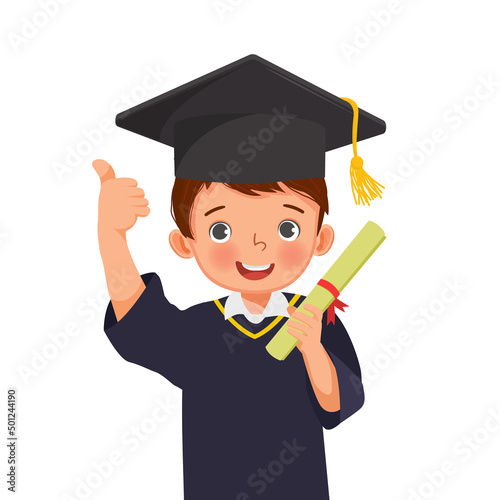 cute little schoolboy in graduation hat and gown holding diploma certificate thumb up
