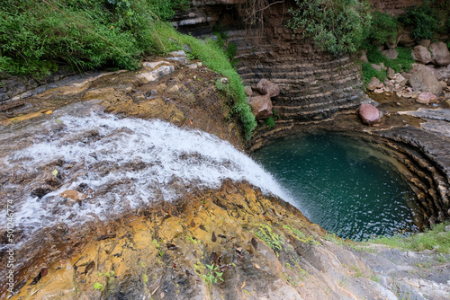 Fototapeta Naklejka Na Ścianę i Meble -  A beautiful flowing waterfall, circular water swimming hole with turquoise water surrounded by cascade rocks in the districts, a popular tourism spot, East Timor