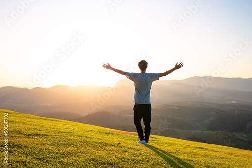 Tableau sur toile Man with arms raised with sunset in the mountains in the background