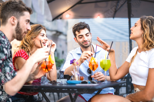 Four trendy young people get together carefree sitting and bonding at outdoors bar restaurant - best friends having fun drinking cocktails at summer aperitif - life style concept - vivid colors