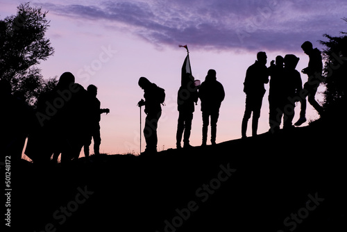 Silhouetted people reach the summit of mountain at dusk with beautiful purple sunrise sky, groups of people reach the top of Mt Ramelau in East Timor, Southeast Asia