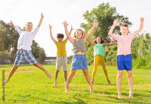 Fotografi Children jumping and raising their hands up togeher outdoors.