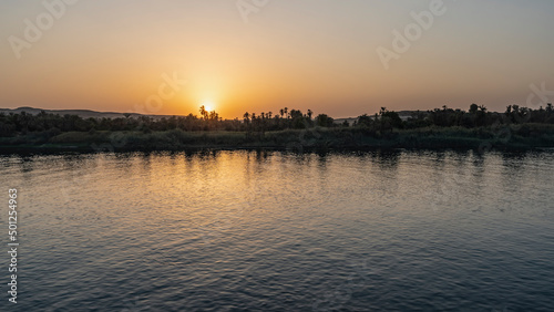 Sunset on the Nile. The sun is low. The sky is colored orange. Reflection and glare on the surface of a calm river. Egypt