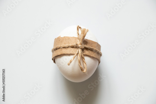 One white chicken egg tied with a rope lies on a white background, Easter holiday