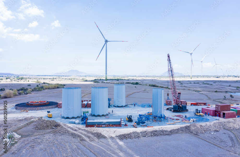 Mobile crane and wind turbine under the blue sky. Wind power plant under construction with several foundations constructed to reduce global warming and climate change