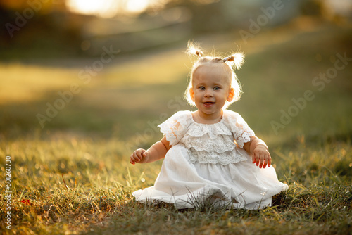 Happy little girl sits on the grass outdoors. Cute baby girl with blond hair is walking in park. Adorable kid play with grass. concept of happy childhood, games, fun. Family leisure. outdoor play © katyagorphoto