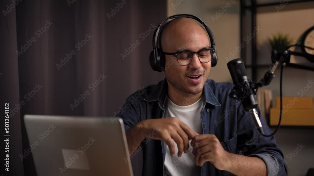 Content creator man host streaming his a podcast on laptop with headphones and microphone interview cheering guest conversation at night broadcast studio. Blogger motivation recording voice over radio Content creator man host streaming his a podcast on laptop with headphones and microphone interview cheering guest conversation at night broadcast studio. Blogger motivation recording voice over radio