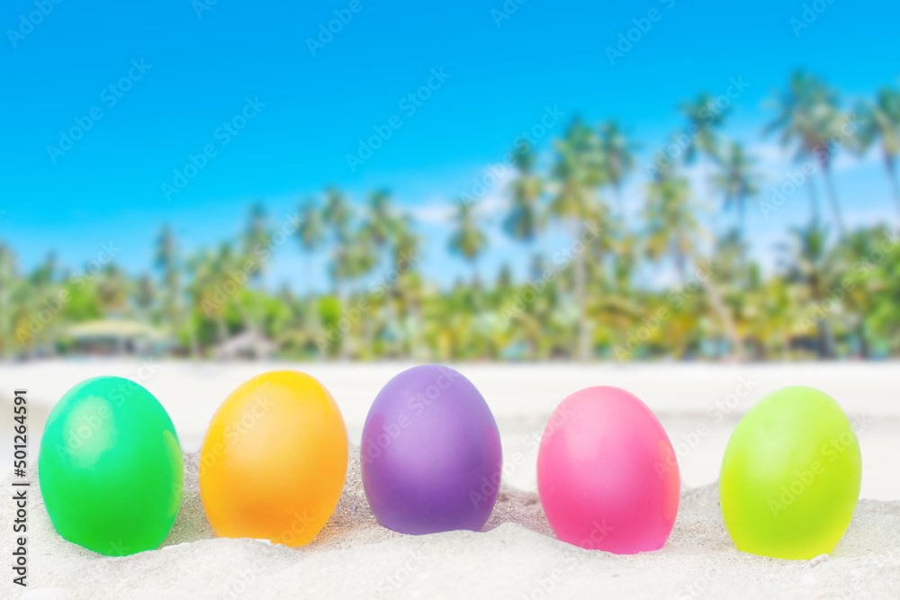 colorful eggs on white sand beach over blue sea background.