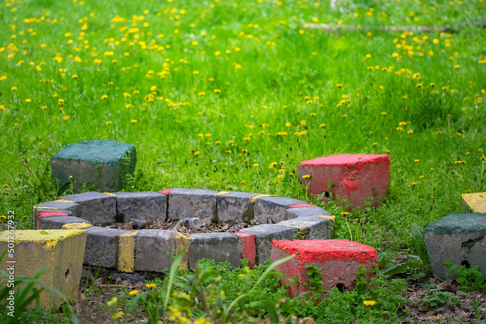 Round stone fireplace  in the garden, and colorful concrete bench in the green grass with yellow flowers