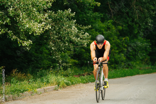 Muscular man riding his racing bike on a road through park with overgrown trees