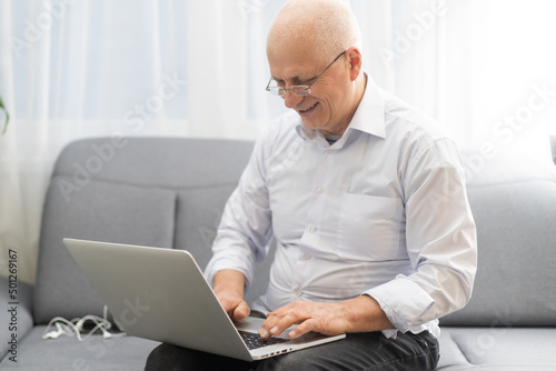 Budget Planning. Pensive Senior Man Using Laptop And Writing In Notebook Sitting At Desk At Home, Empty Space.