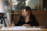 A beautiful Asian businesswoman sitting in her private office, she is checking company financial documents, she is a female executive of a startup company. Concept of financial management.