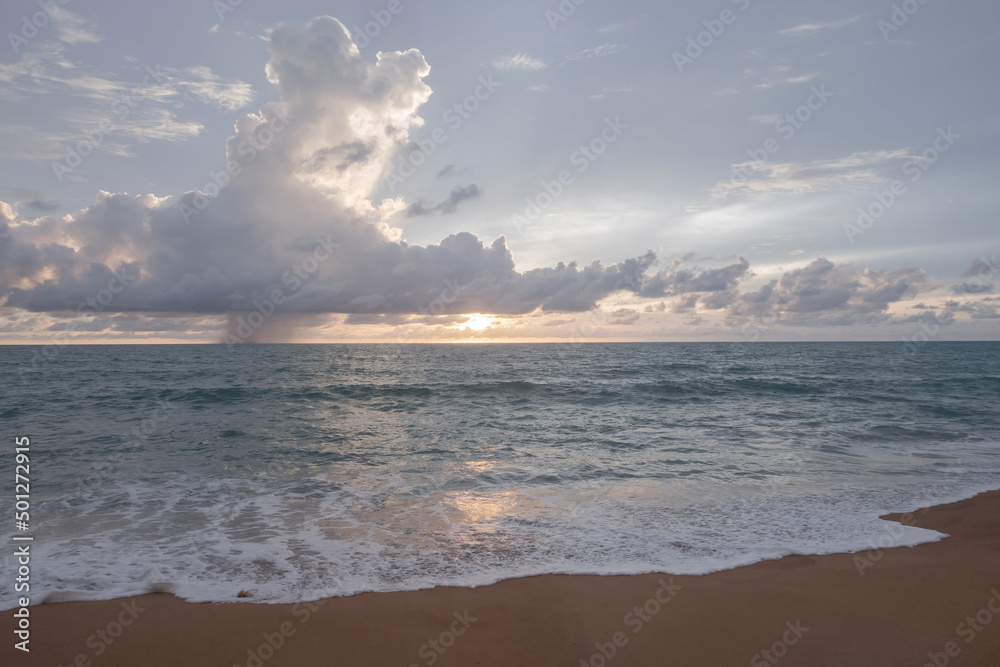Cloudy afternoon and sunset with the sea and waves crashing on the sandy beach.