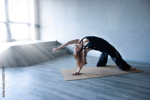 Yoga a woman practices asanas in black clothes by the window. Volumetric rays of sven through the window photo