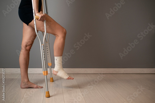 Woman with injured leg using crutches on grey background, closeup. Space for text