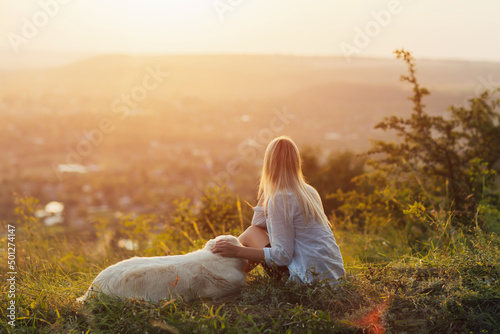 A beautiful girl hugs her golden retriever on the mountain. Young woman with a dog at sunset.