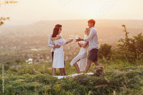 Beautiful happy people enjoy white wine on picnic date in beautiful setting at nature. Romantic getaway for friends.