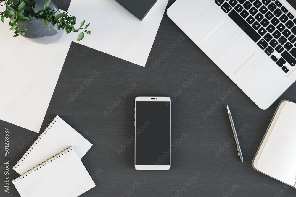Smartphone with blank screen is on top of dark wooden office desk table with laptop computer and supplies, above view. Mock up, 3D Rendering. Smartphone with blank screen is on top of dark wooden office desk table with laptop computer and supplies, above view. Mock up, 3D Rendering.