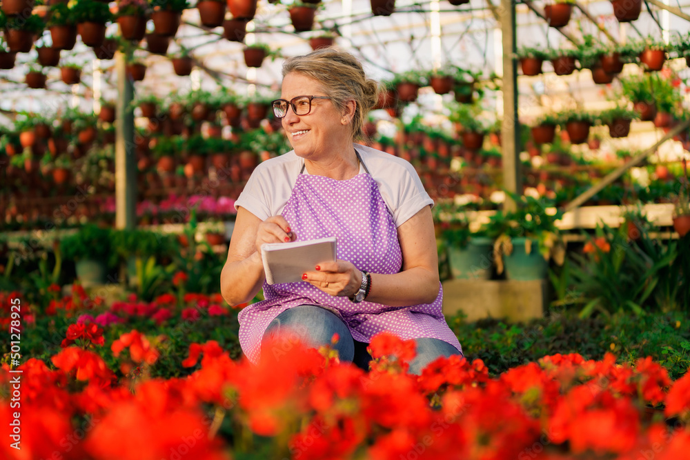 Senior woman owner of small business with flowers checking her plants while using notebook for note everything she need.