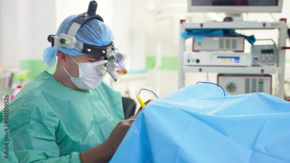 Busy male doctor with device glasses on head operating the patient. Specialist holds an instrument and takes a large syringe. Busy male doctor with device glasses on head operating the patient. Specialist holds an instrument and takes a large syringe.