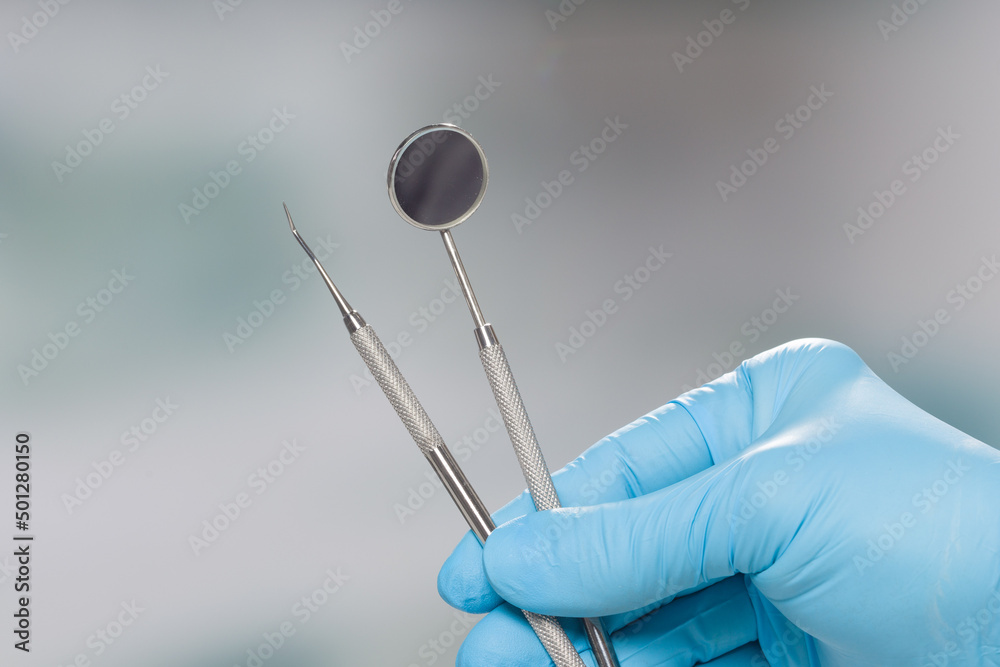 Close up of dentist's hand in blue gloves presenting dental instruments Close up of dentist's hand in blue gloves presenting dental instruments