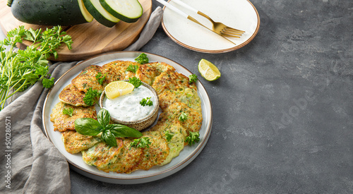 Zucchini pancakes with herbs and sour cream on a blue plate. Vegetarian dish on the gray background, copy space for text