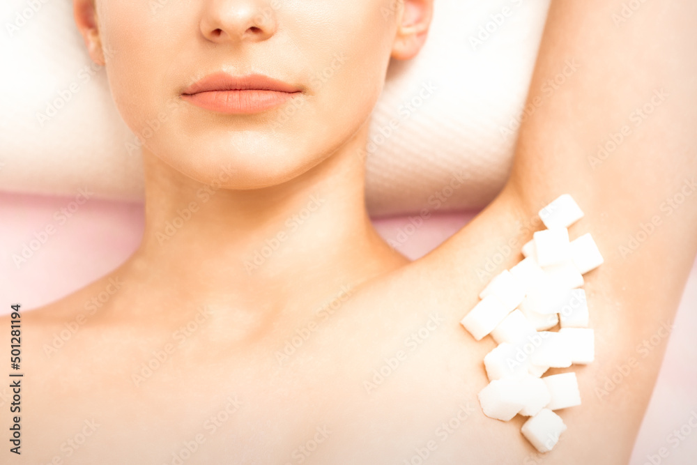 Sugaring, waxing concept. White sugar cubes lie down on the female armpit of the young white woman, close up Sugaring, waxing concept. White sugar cubes lie down on the female armpit of the young white woman, close up