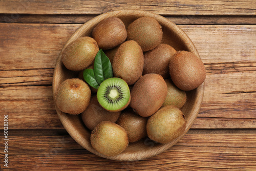Bowl with cut and whole fresh kiwis on wooden table, top view