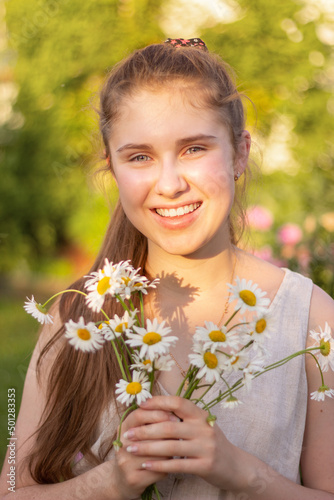 A beautiful young girl smiles at the camera and holds a bouquet of flowers in her hands. Vertical
