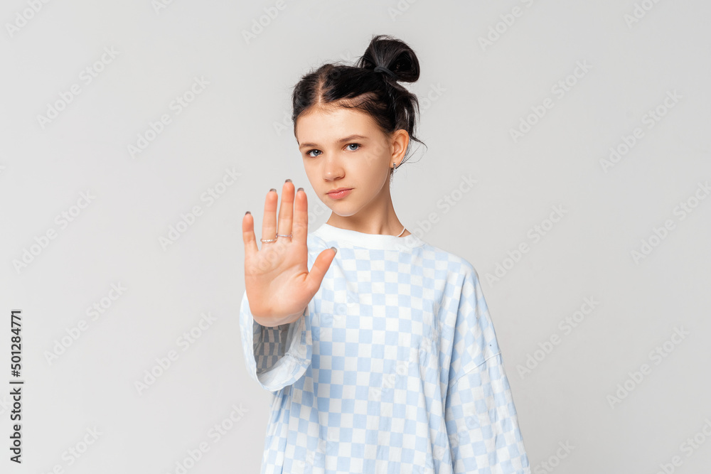 Please, do not, stop. Serious dark-haired teen girl, who is looking in the camera and extends arm in stop sign, standing in trendy t shirt over light grey background. Stay home. Social distancing Please, do not, stop. Serious dark-haired teen girl, who is looking in the camera and extends arm in stop sign, standing in trendy t shirt over light grey background. Stay home. Social distancing