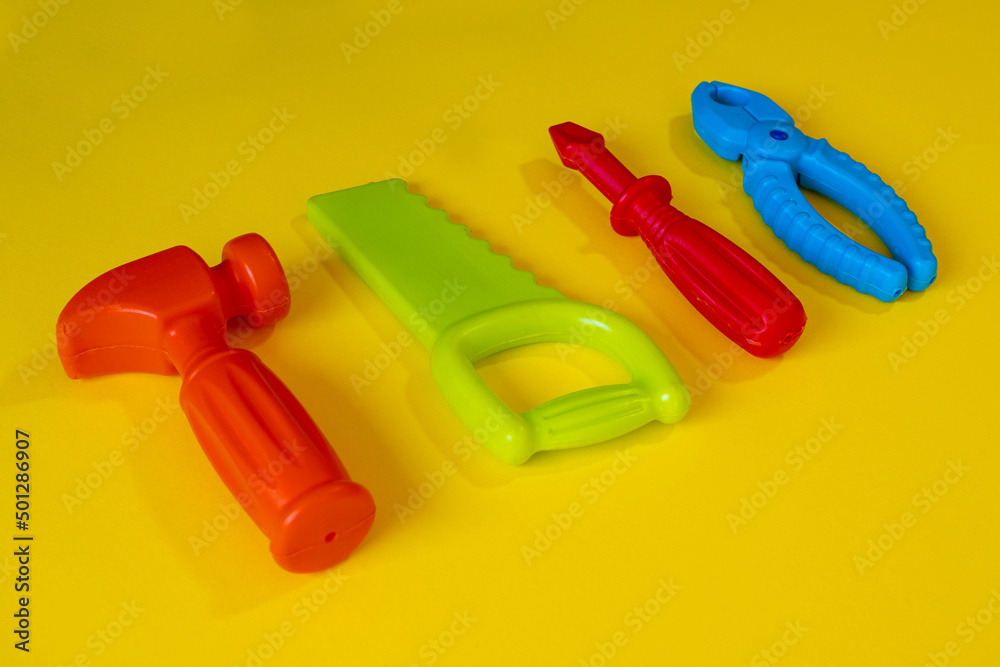 Colorful repair toys on yellow background, child's play isolated on yellow backdrop, playing idea, colored screwdriver pliers saw hammer, side view Colorful repair toys on yellow background, child's play isolated on yellow backdrop, playing idea, colored screwdriver pliers saw hammer, side view