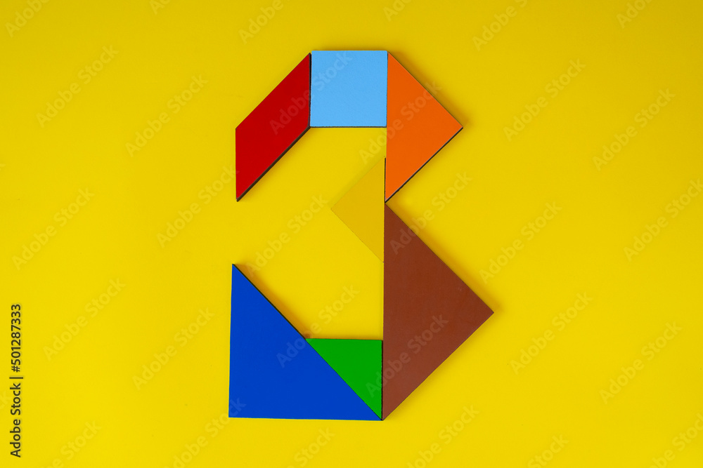 Fototapeta premium Colorful number 3 made with tangram toy, colored tangram number three isolated on yellow background, kids game idea, teaching counting for children, puzzle toy, top view of third numeric