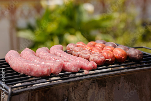 Man cooking botifarra sausage and black pudding on the barbecue grill for an outdoor summer party. Barbecue smoke. Background of food.