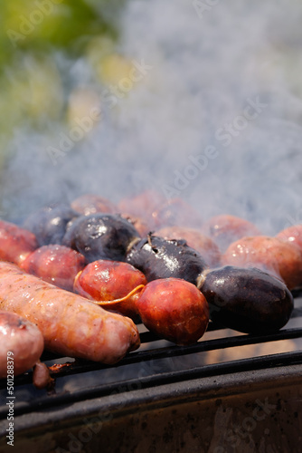 Man cooking botifarra sausage and black pudding on the barbecue grill for an outdoor summer party. Barbecue smoke. Background of food. Vertical Shot.