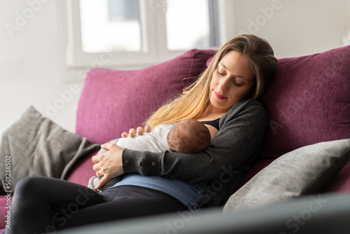 Young mother on the sofa breastfeeding her newborn baby