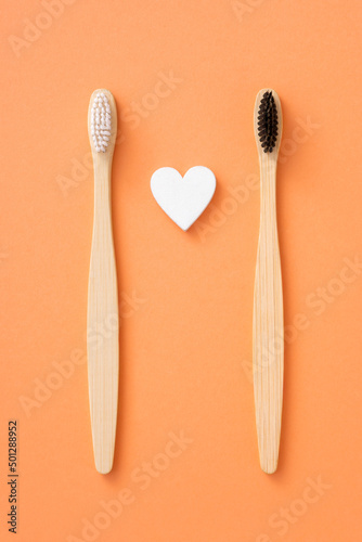 Two bamboo dental brushes and heart on orange background for Valentine day. Couple of wooden toothbrushes. Teeth health concept.