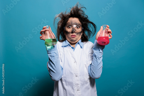 Obraz na płótnie Mad chemist with dirty face and messy hair having flasks filled with unknown chemical substances