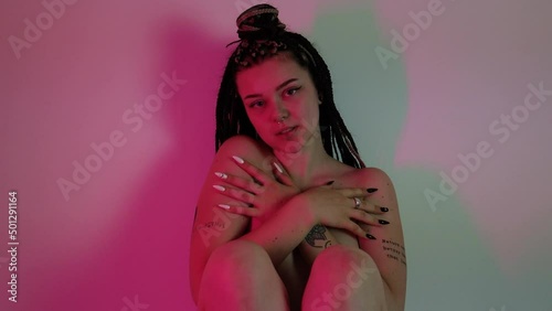 Seductive young woman with braided hair teasing in pink lighting