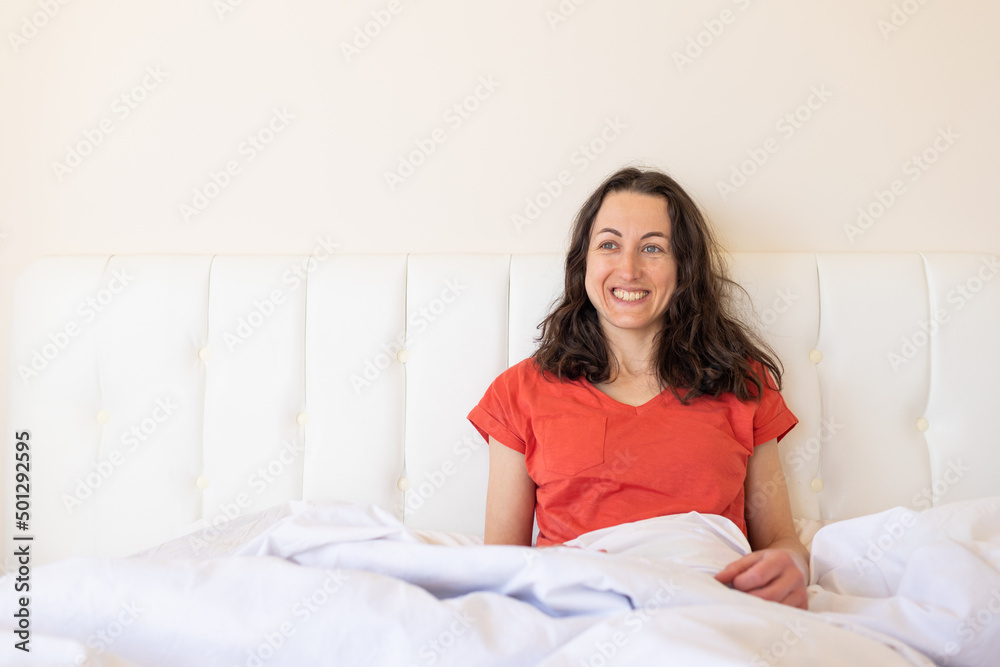 A girl in red pajamas sits on a white bed