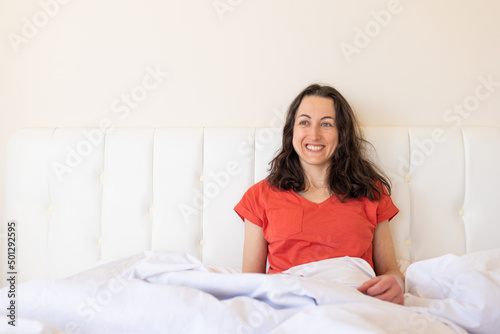 A girl in red pajamas sits on a white bed © zhukovvvlad